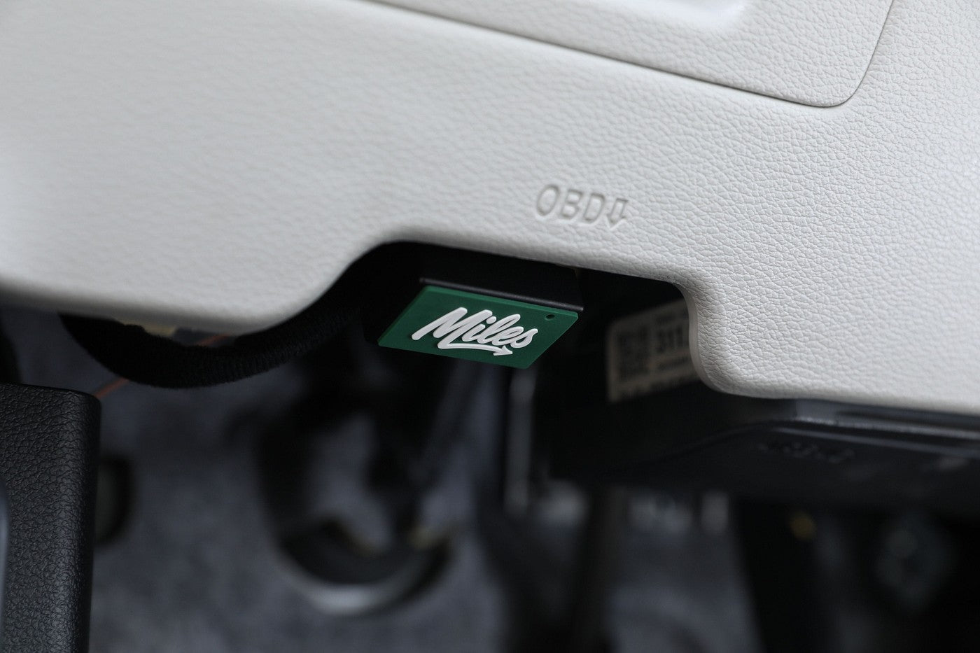 Miles Plug seated in the diagnostic port under a car dashboard.
